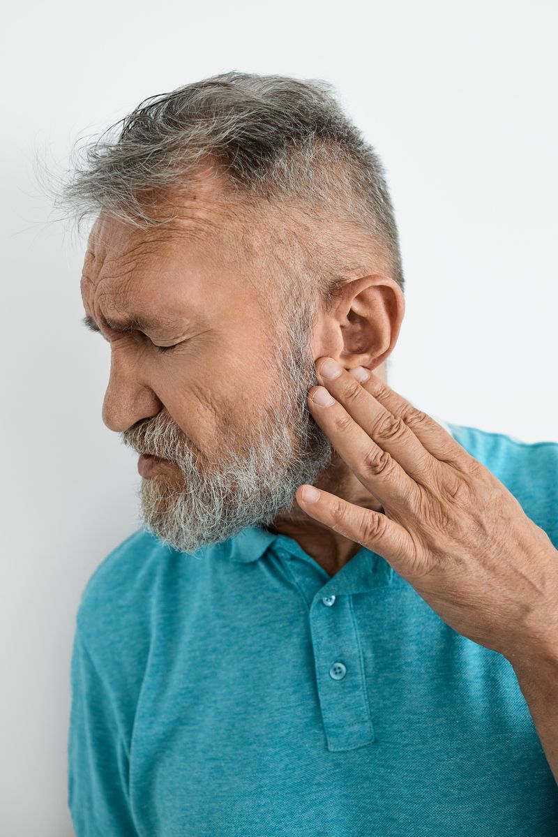Man in a teal shirt touching his jaw, appearing to feel pain or discomfort.
