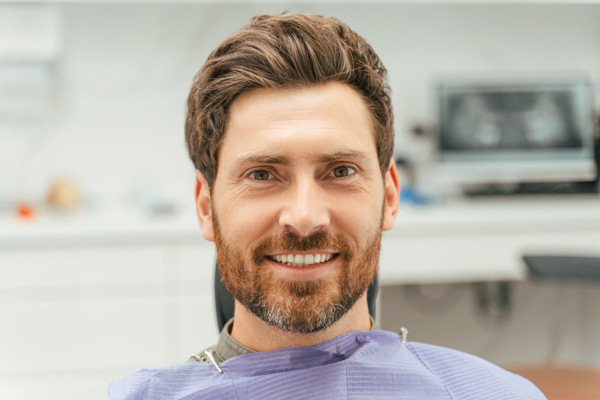Smiling man in a purple dental bib seated in a bright clinic room