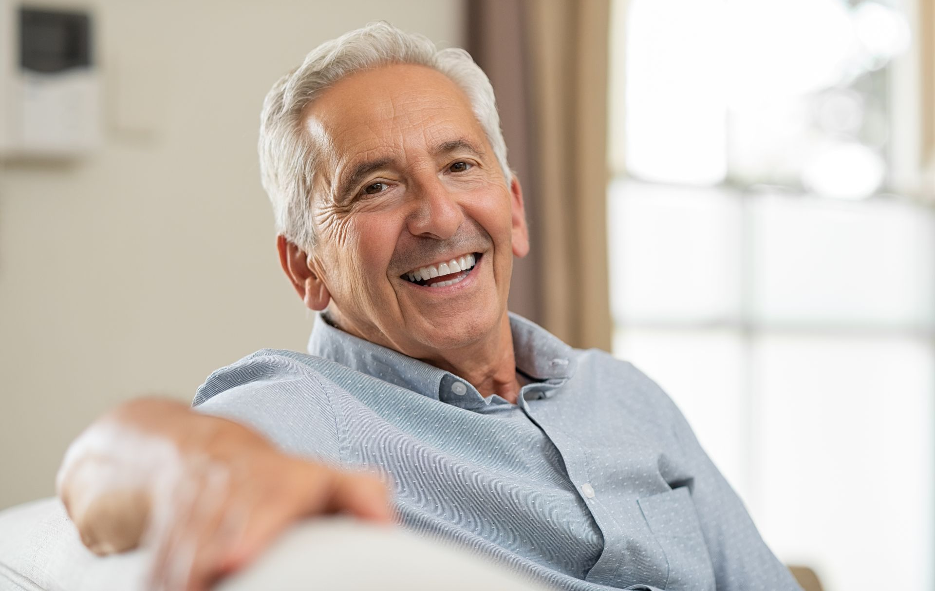 Smiling older man in a light blue shirt sitting on a couch in a bright room