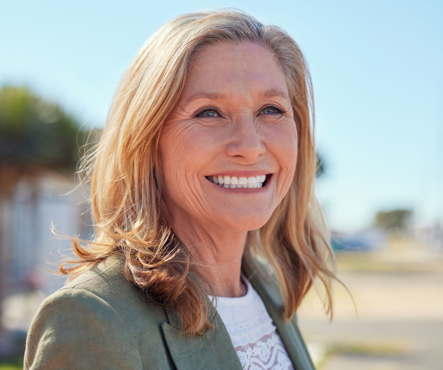 Smiling woman outdoors in a green jacket with blurred beach background