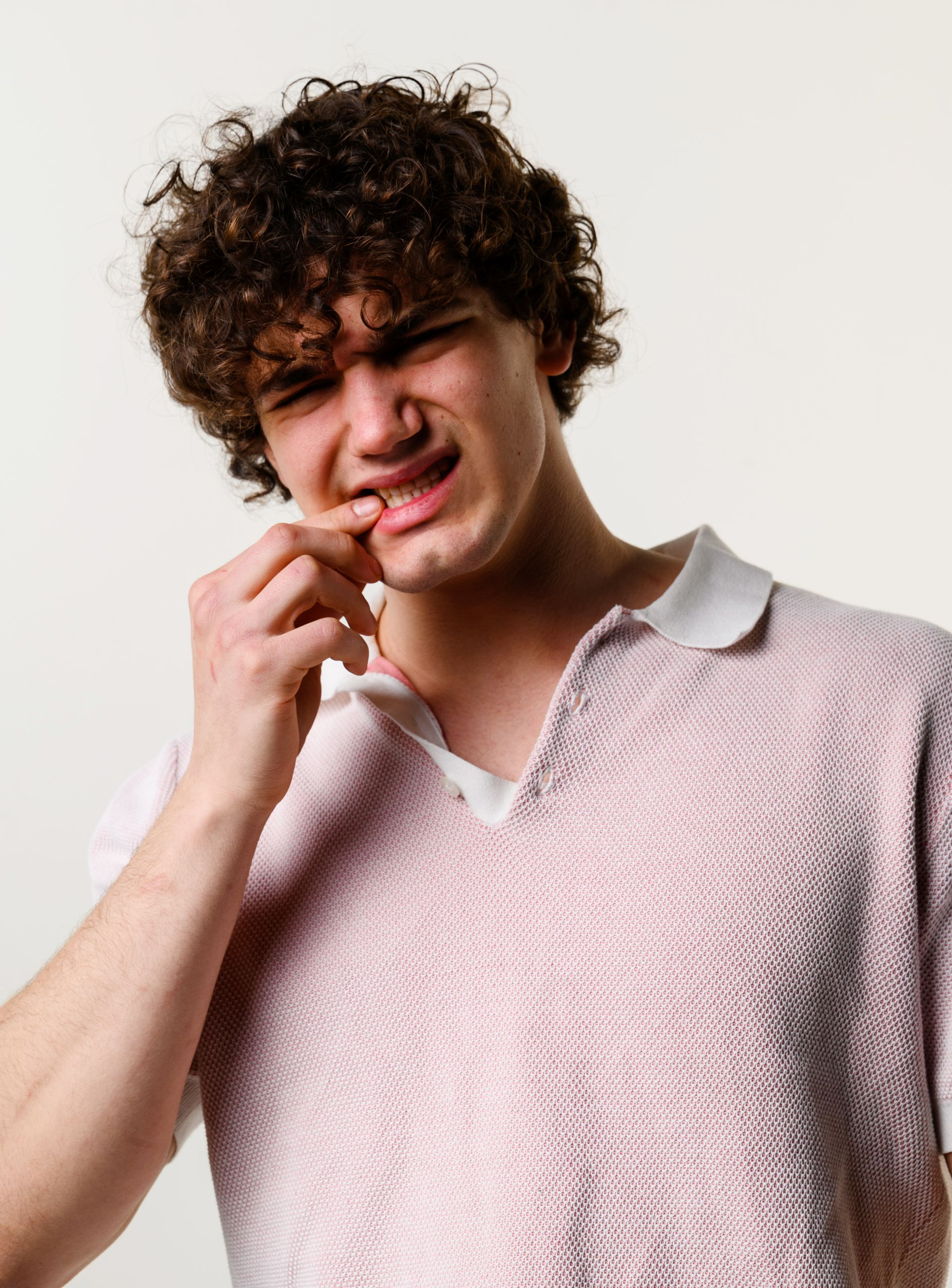 Person with curly hair pinching their lip, wearing a light pink sweater against a plain background