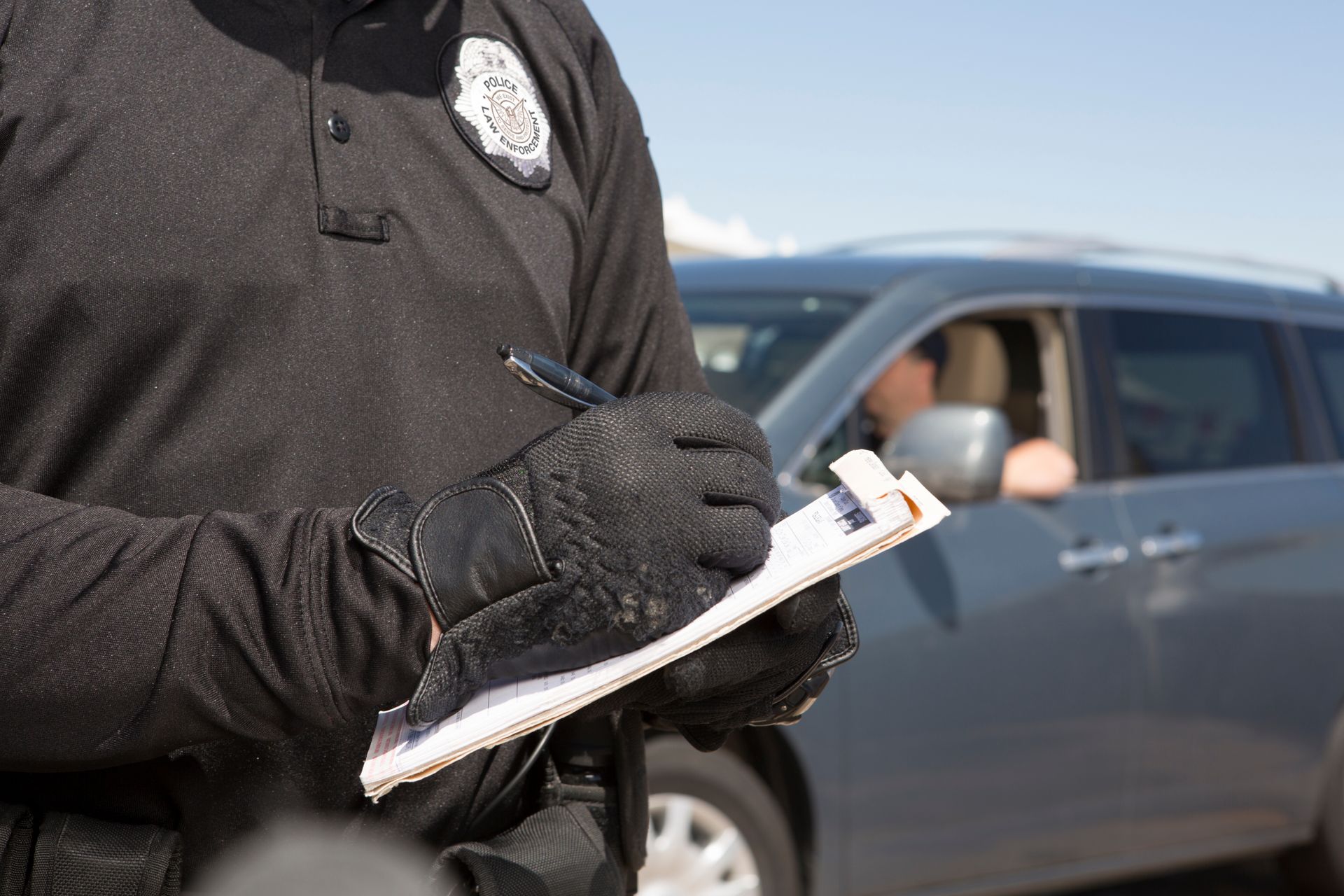Police officer writing a ticket beside a gray car on a roadside