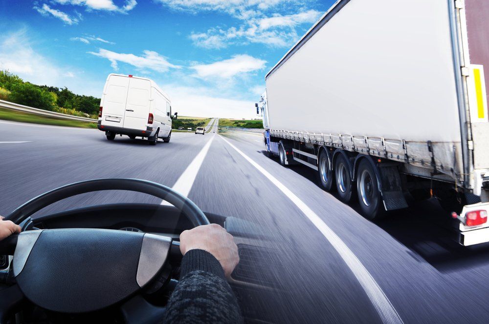 Driver's view of a highway with a white van ahead and a semi-truck passing on the right