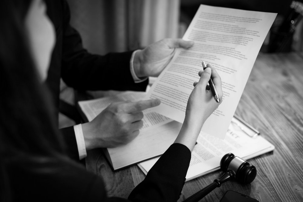 Two people review and sign a document at a desk with a gavel nearby.