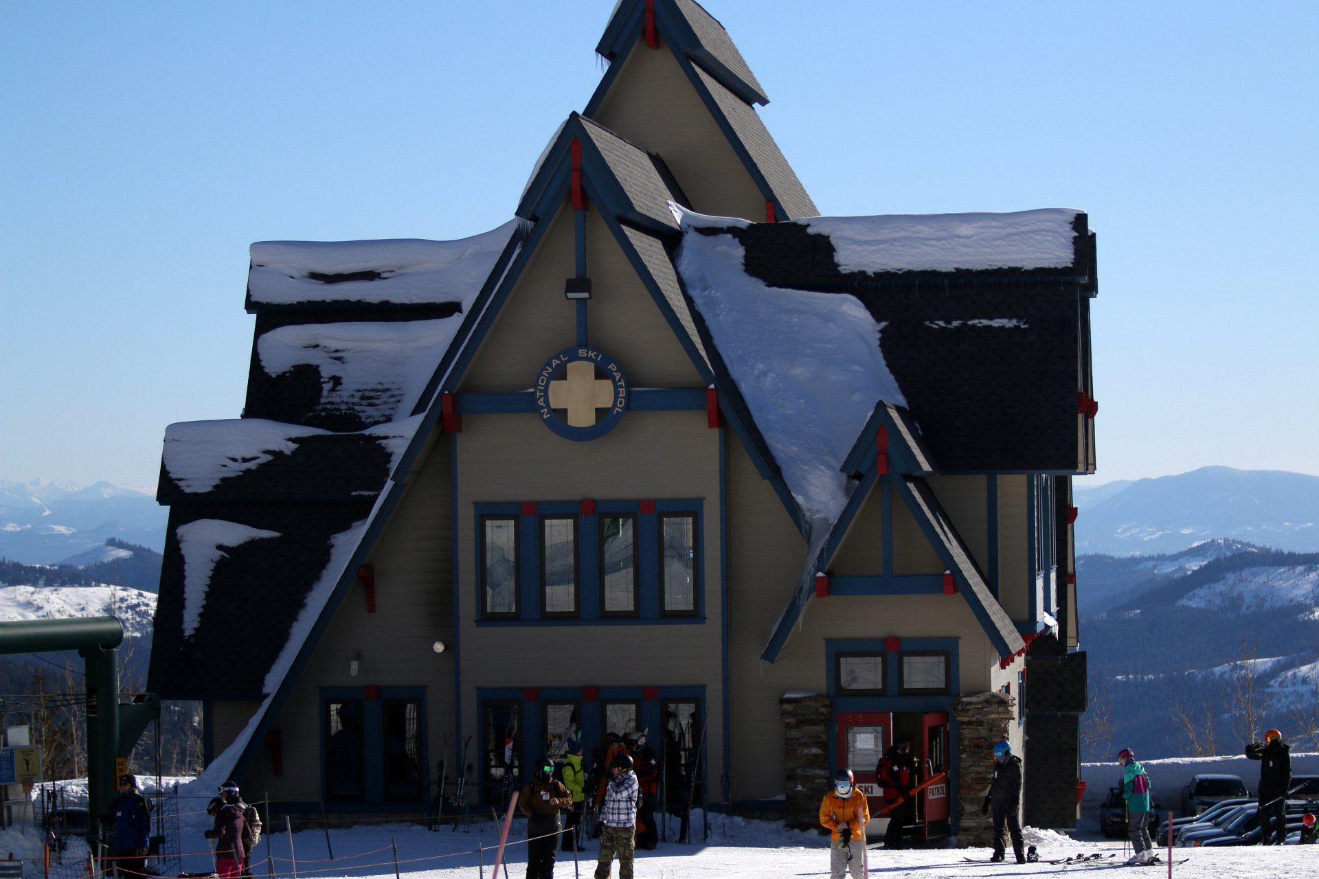 Snow-covered alpine lodge with people outside under a clear blue sky