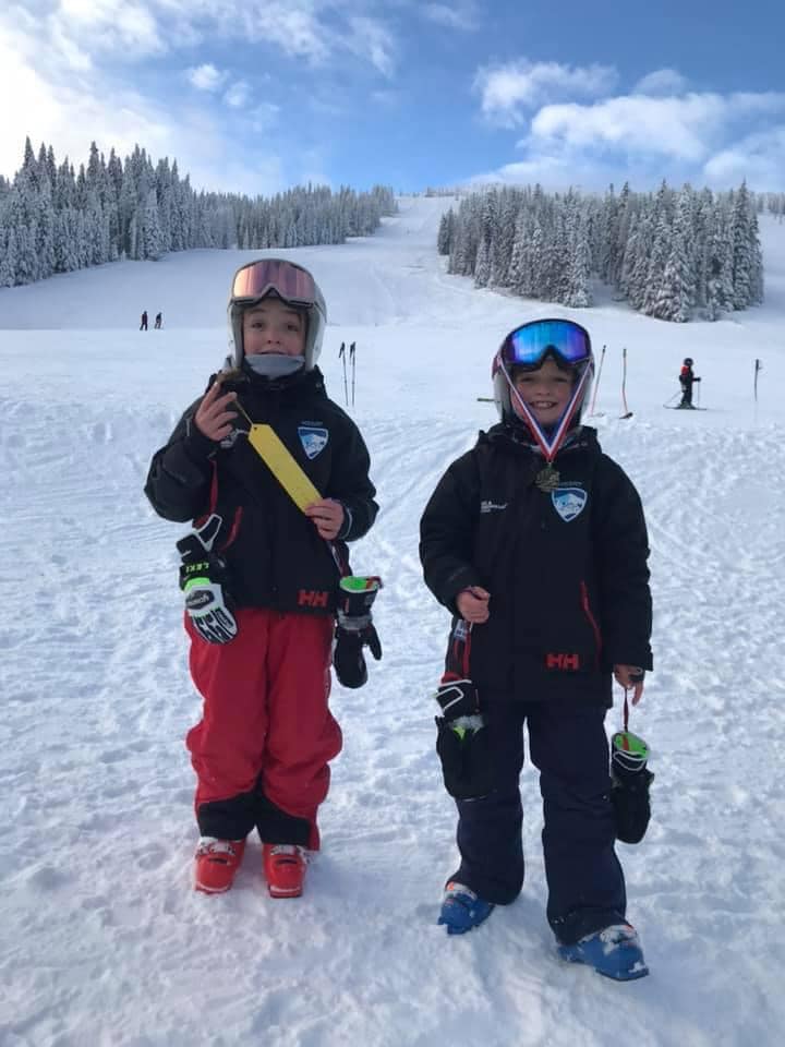 Two skiers in helmets and goggles standing on a snowy slope with trees in the background