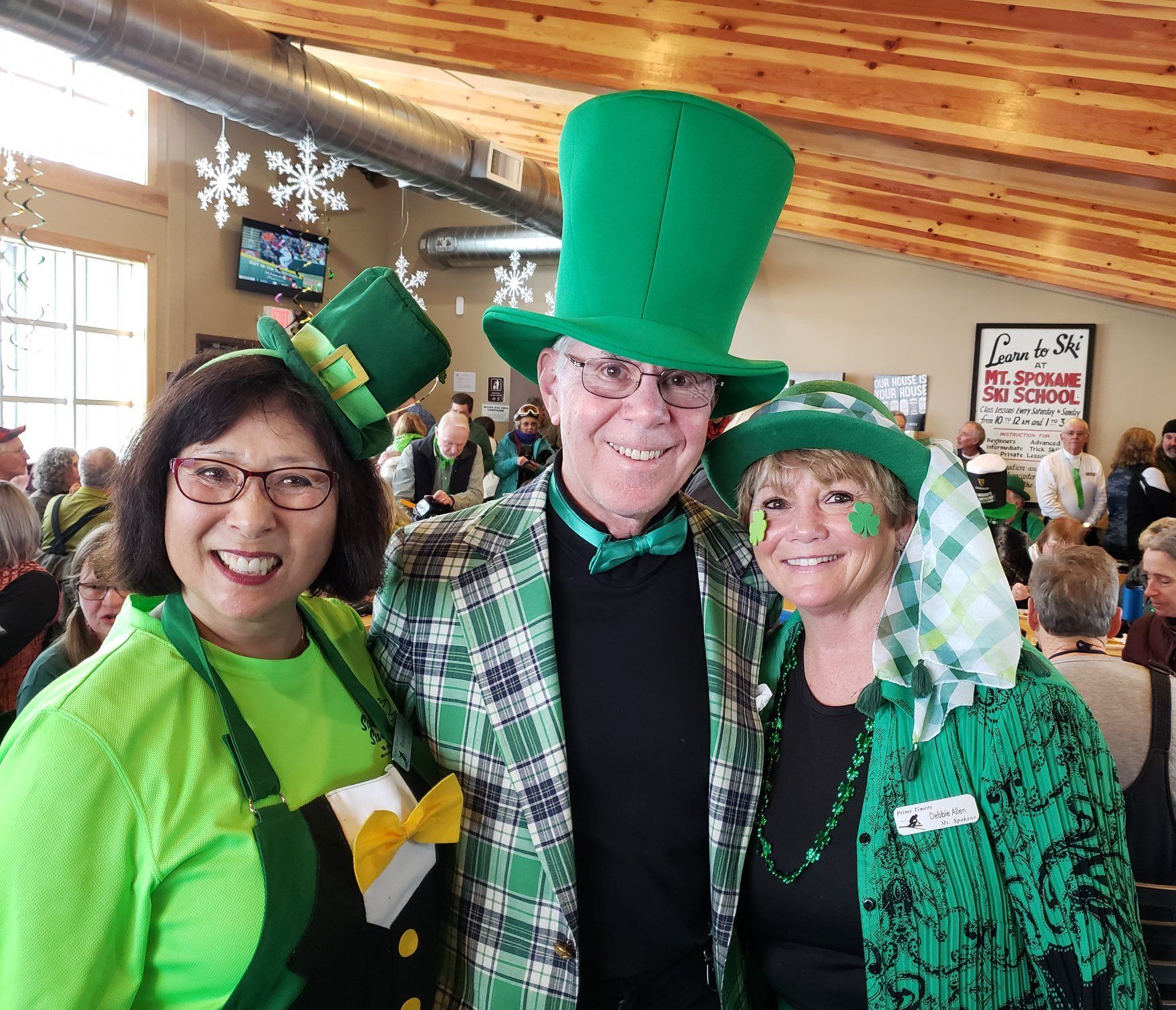 Three smiling people in green St. Patrick’s Day outfits at an indoor event