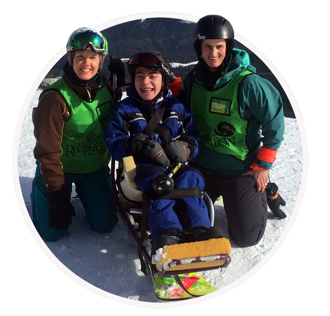 An Adaptive Skier shown in a Sit Ski, posing for a picture with two other people