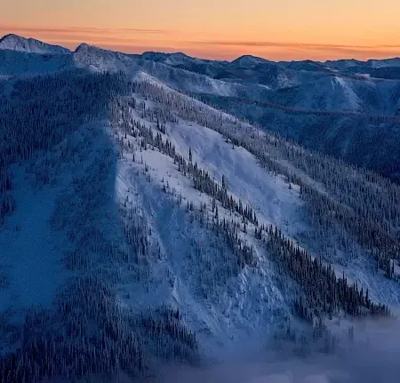 An aerial view of Whitewater Mountain covered in snow at sunset.