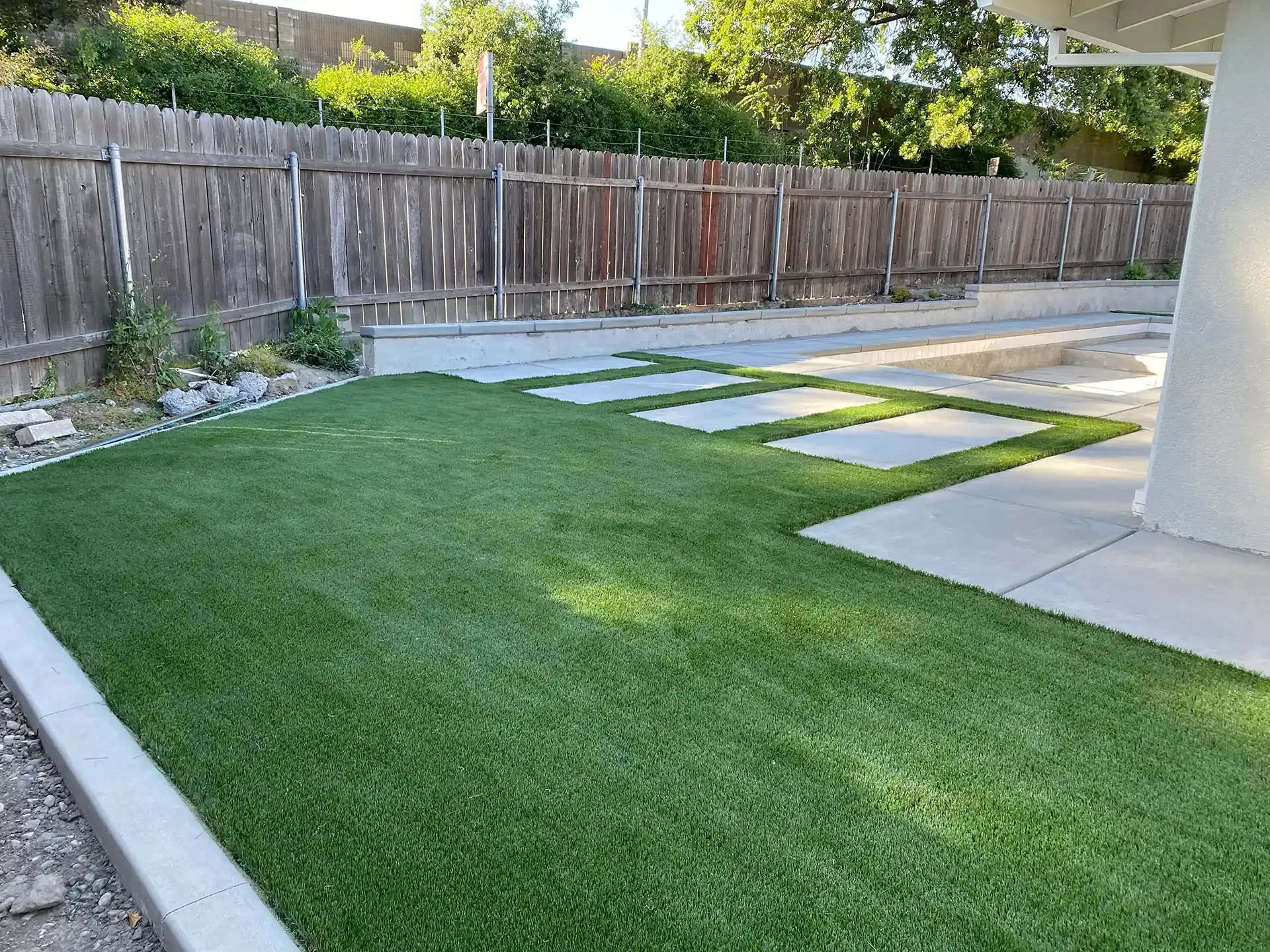Artificial turf and concrete patio in backyard with wooden fence.