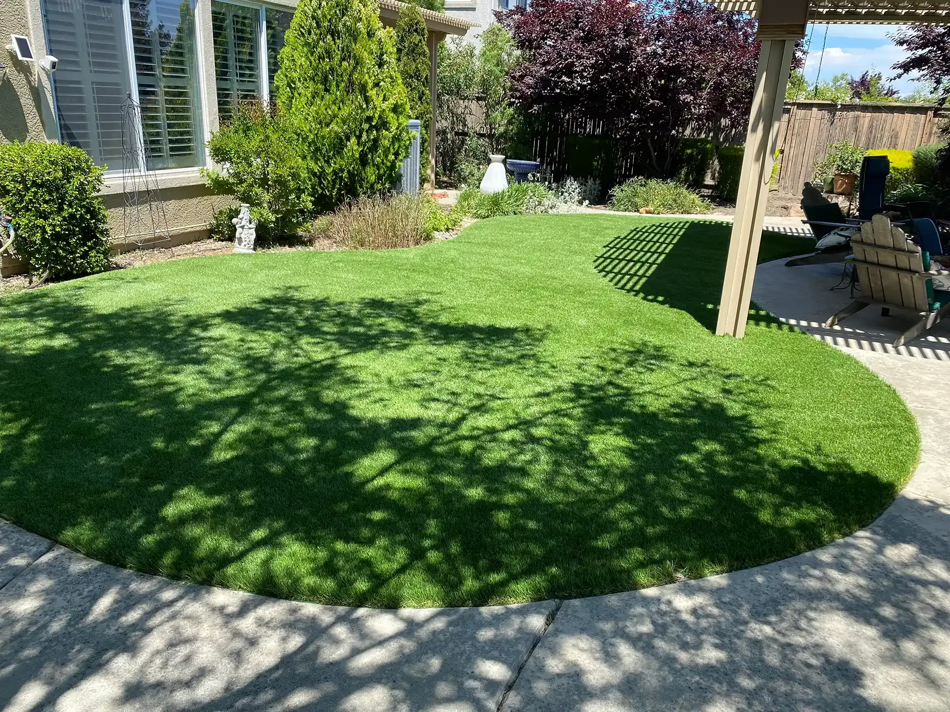 Green artificial turf in backyard, surrounded by concrete patio and plants.