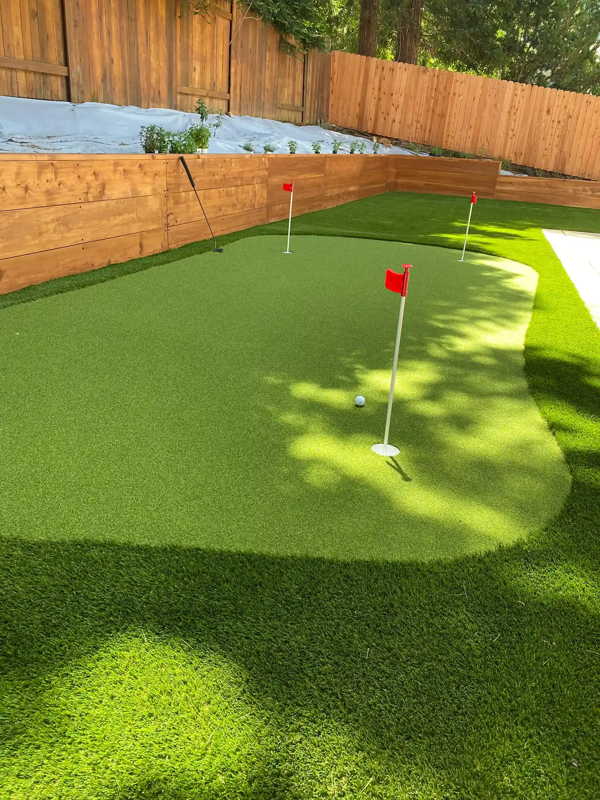 Artificial turf putting green in a backyard with wooden fence. Flags mark the holes.