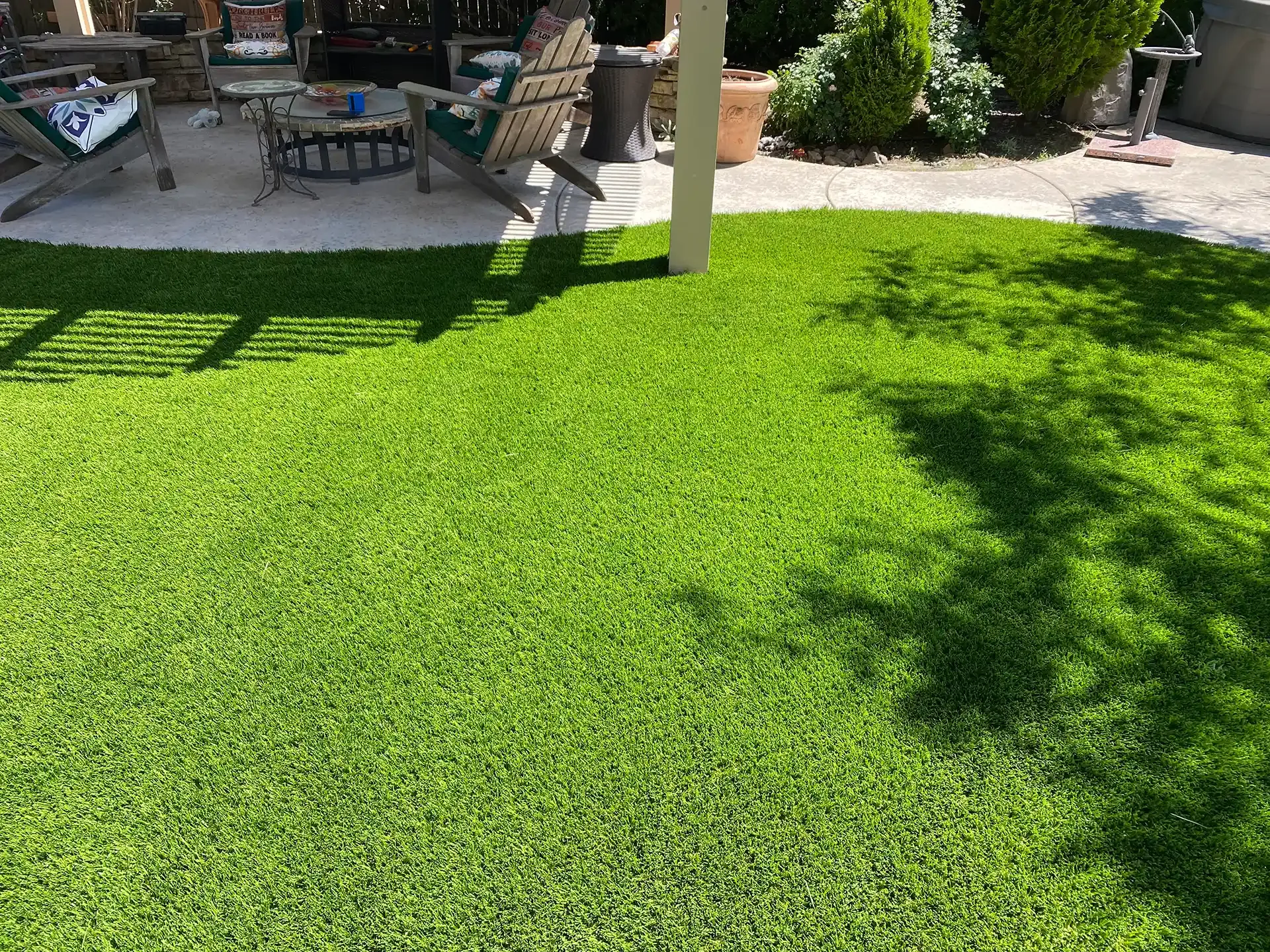 Bright green artificial turf lawn in a backyard, with a patio and shaded area in the background.
