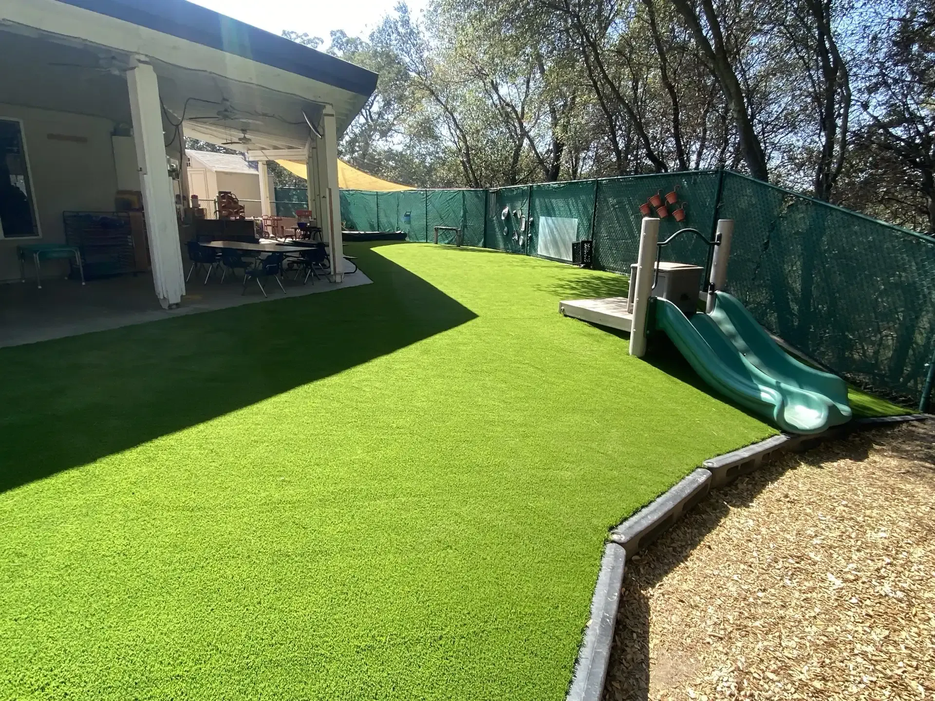 Playground with green turf, slide, and covered patio.