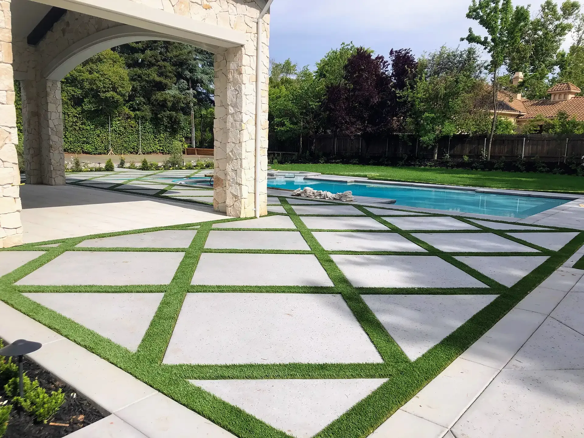 Patio with geometric concrete squares separated by green turf, leading to a pool.