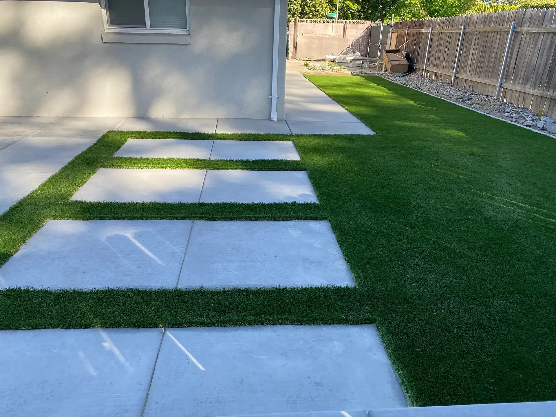 Concrete pavers with green grass in between, adjacent to a lawn and fence.