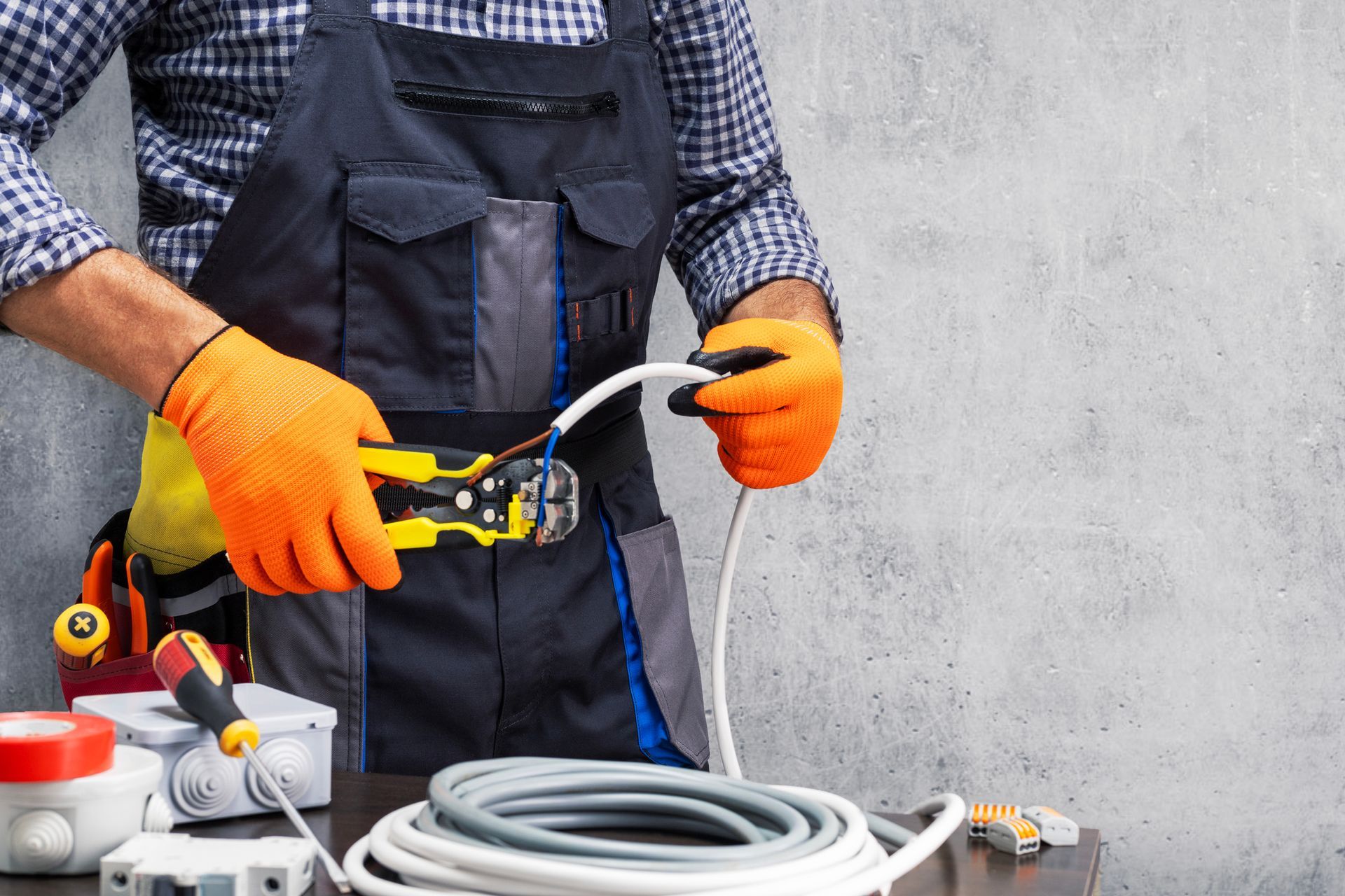 Electrician wearing a tool belt, working on an electrical panel outside a white house on a sunny day.