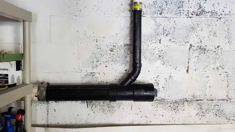 Black pipe system against a white concrete block wall in a basement.
