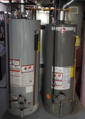 Two water heaters are sitting next to each other in a basement.