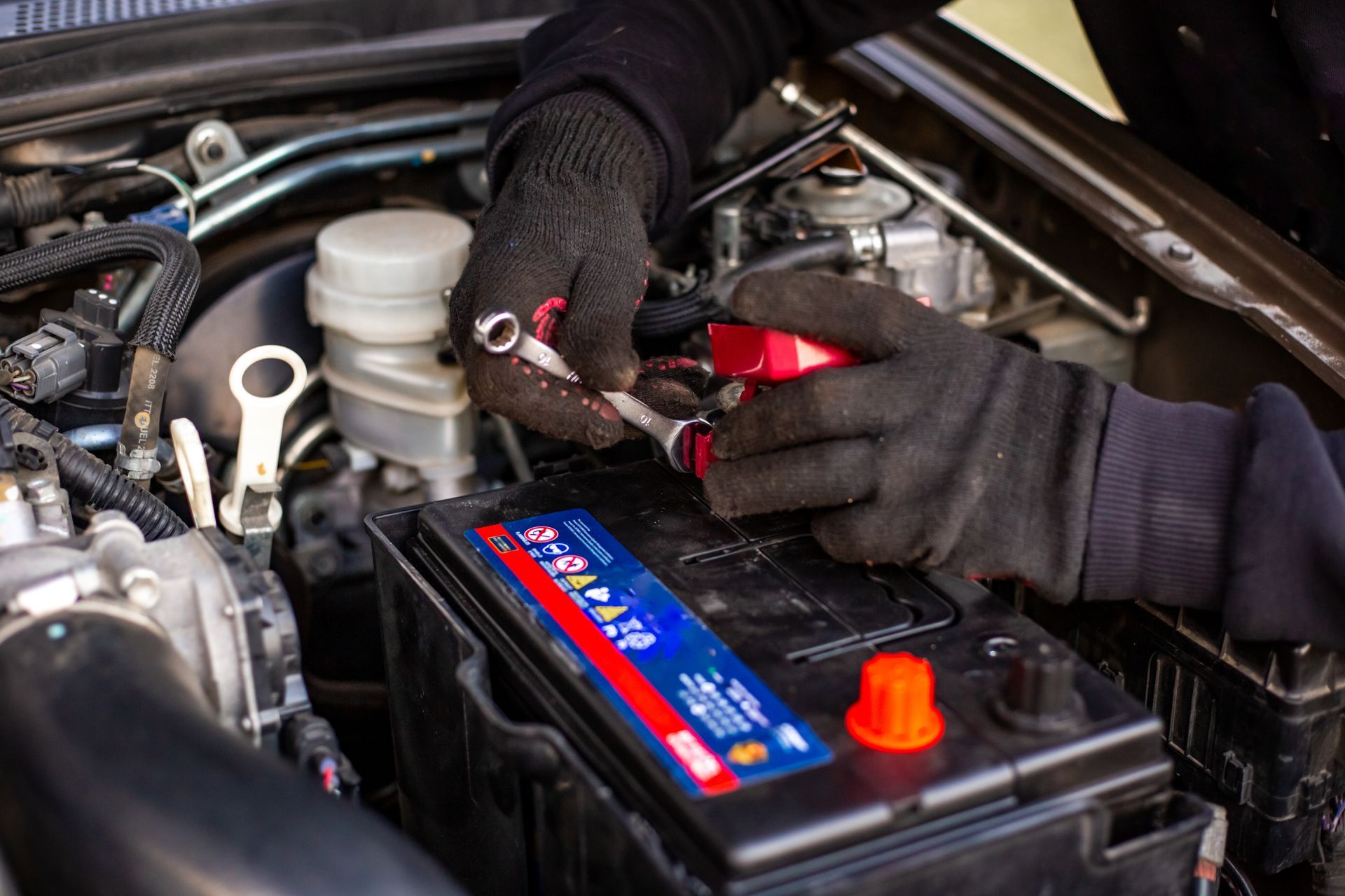 Gloved hands using jumper cables on a car battery under the hood