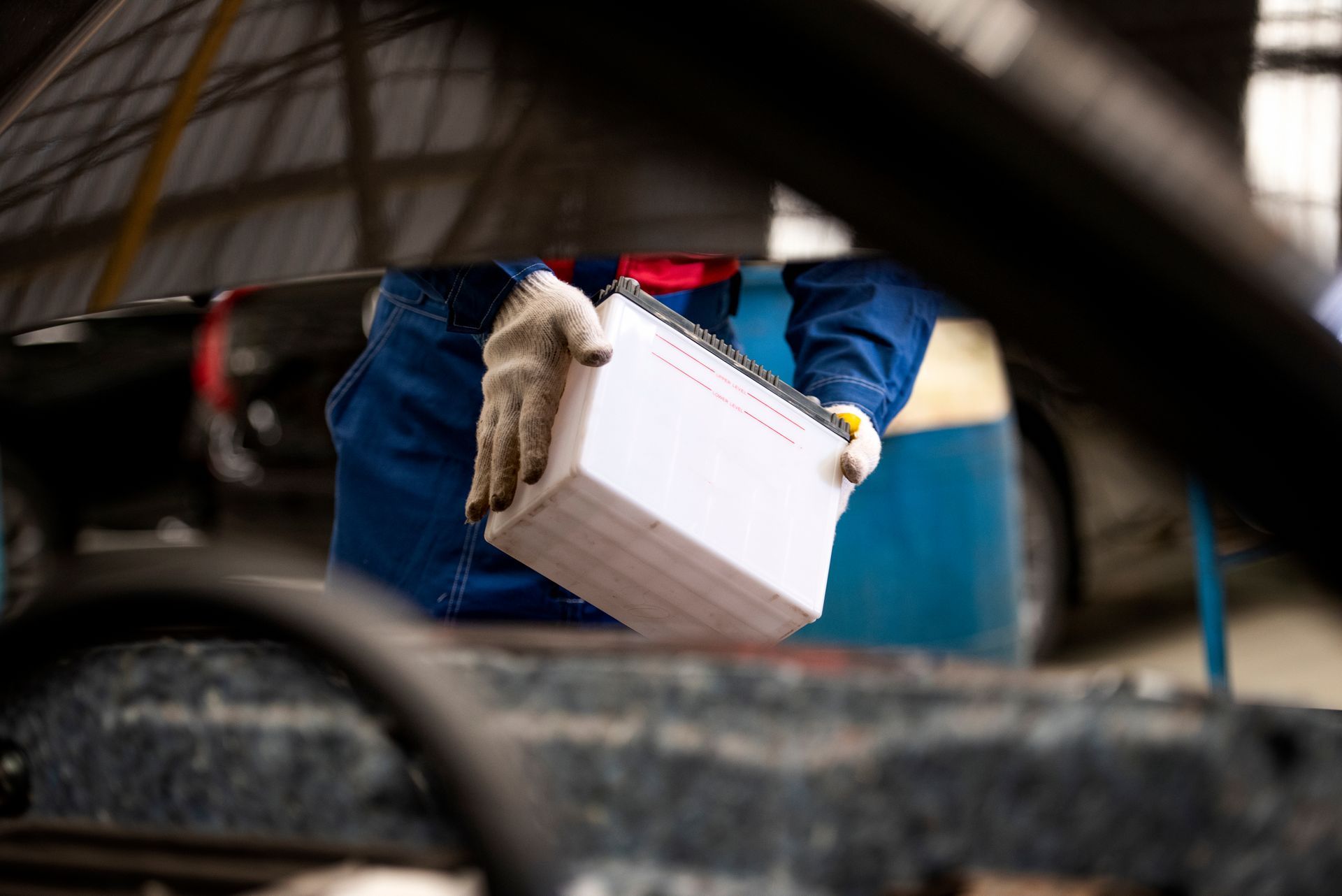 Gloved worker carrying a white box near a car in a garage