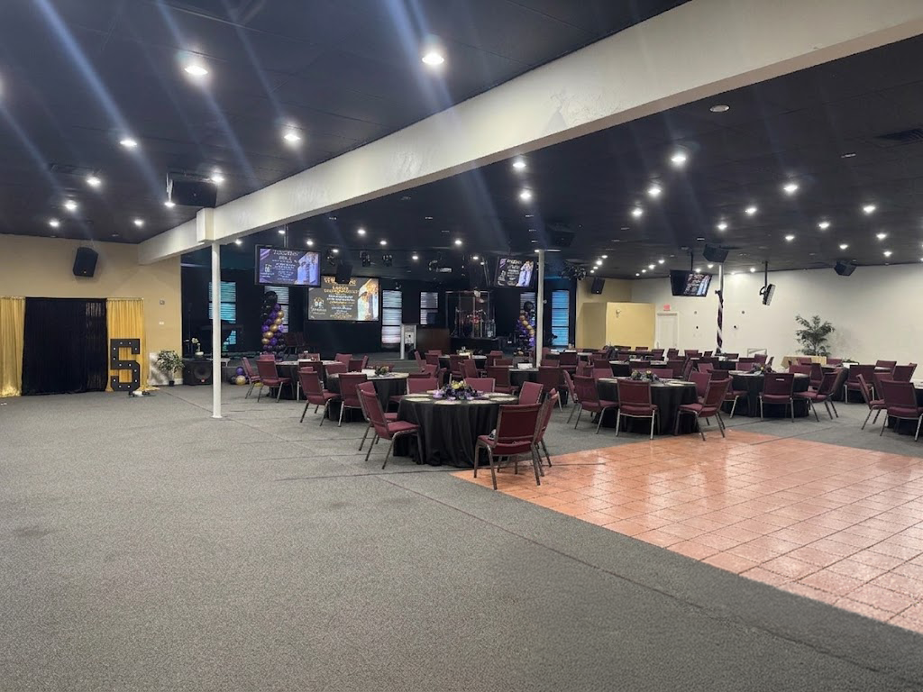Spacious banquet hall with round tables, red chairs, and a tiled dance floor under bright ceiling lights