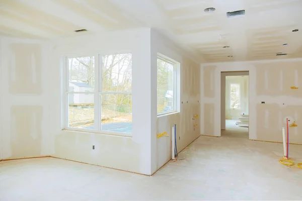 Interior of a room under construction, with drywall walls, windows, and exposed studs.