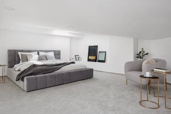 Gray bedroom with a bed, chair, and side tables on a gray carpet.
