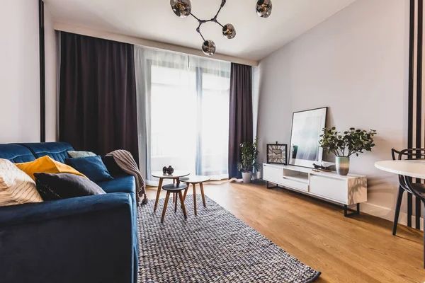 Living room with blue sofa, white console, dark curtains, and light wood flooring.