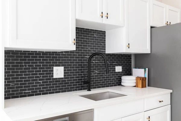 White kitchen with black backsplash, sink, and cabinets.