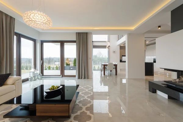 Modern living room with large windows, light tile floors, and a decorative chandelier.