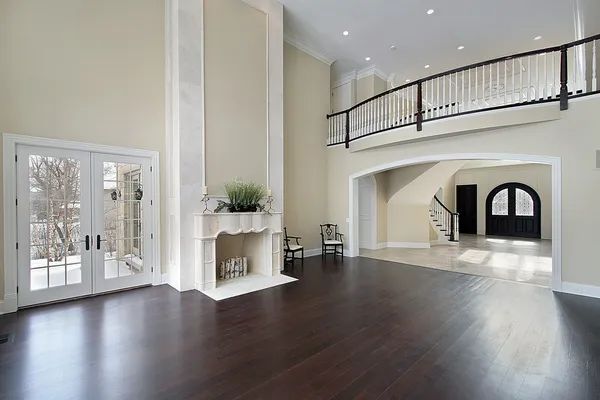 Spacious, bright living room with dark wood floors, fireplace, balcony, and double doors.