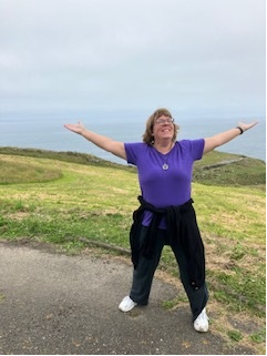 Missy Barnes with arms outstretched on a coastal cliff overlook