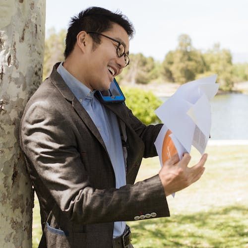 A man leaning on a tree answering a phone while holding a bunch of papers at Overseas Filipino Workers An image man leaning on a tree answering a phone while holding a bunch of papers