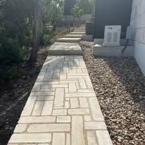 A brick walkway leading to a house surrounded by gravel and trees.