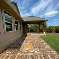 A brick walkway leading to a house with a porch.