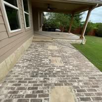 A brick walkway leading to a covered patio in front of a house.