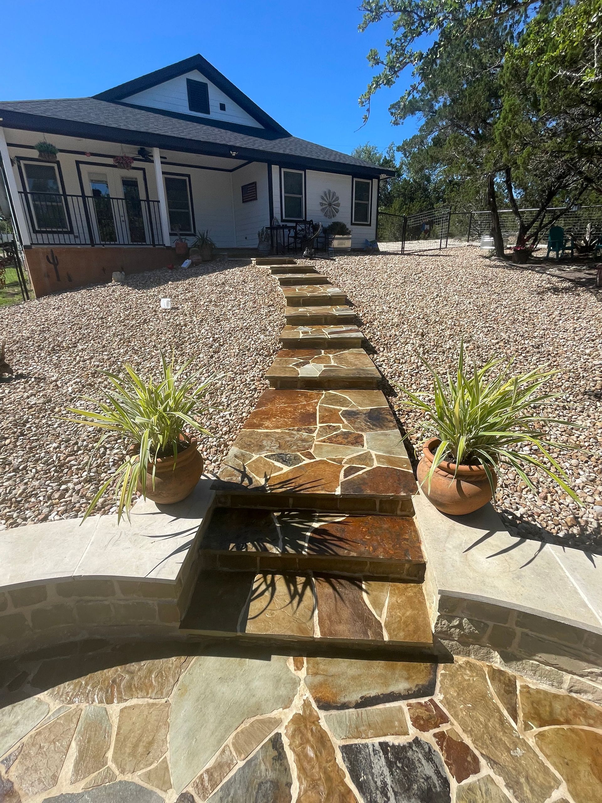 A stone walkway leading to a house with potted plants on the side.