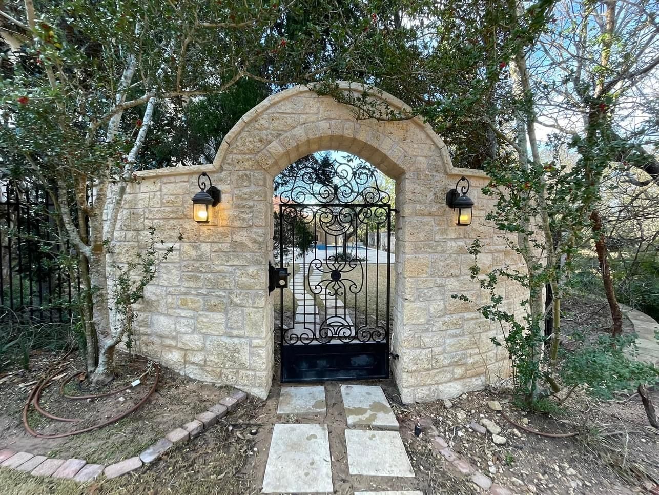 A stone wall with a wrought iron gate leading to a garden.