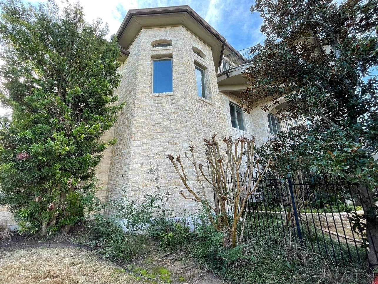 A large brick house with a fence and trees in front of it.