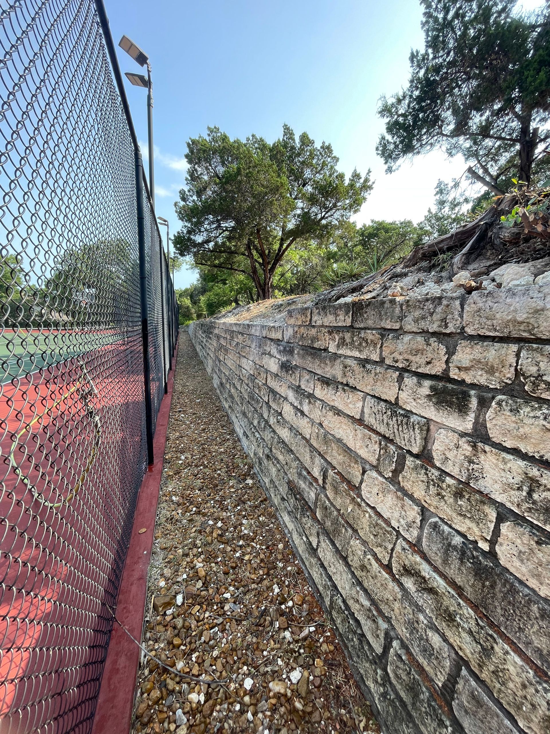 There is a brick wall along the side of a tennis court.