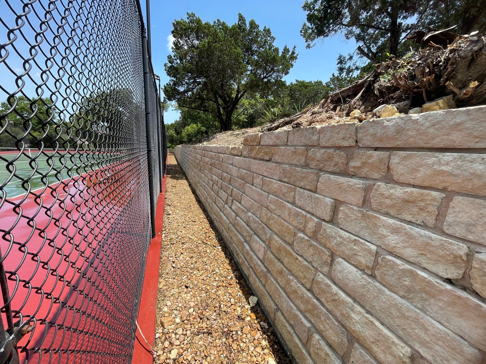 A brick wall next to a tennis court with a chain link fence