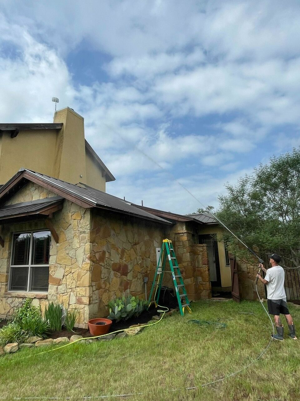 A man is cleaning the roof of a house with a hose.