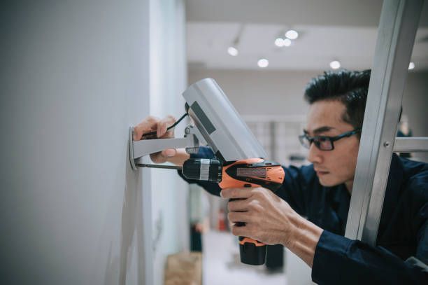 An Asian mid adult man climbs up a ladder installing a security camera