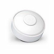 White, circular motion sensor with a raised center, tilted on a white surface.