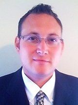 Man in glasses, dark suit, white shirt, and patterned tie.