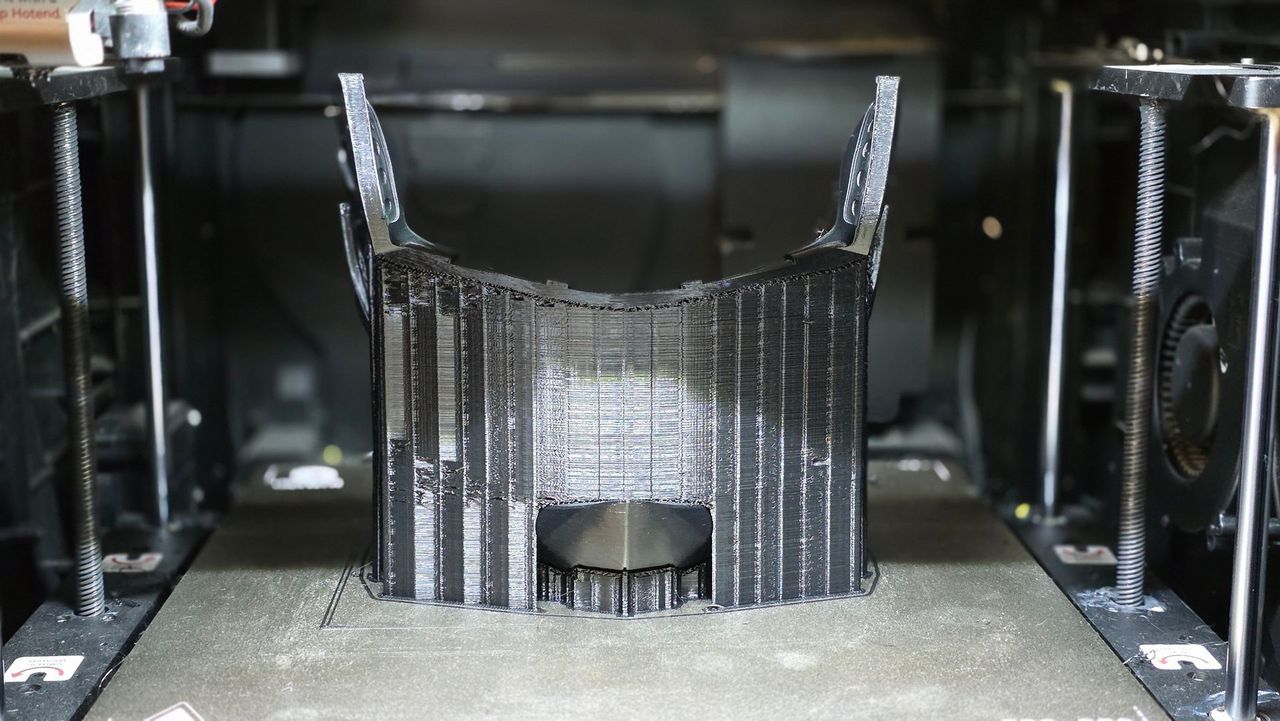 Black PETG helmet chin piece fresh off the 3D printer bed with support structures