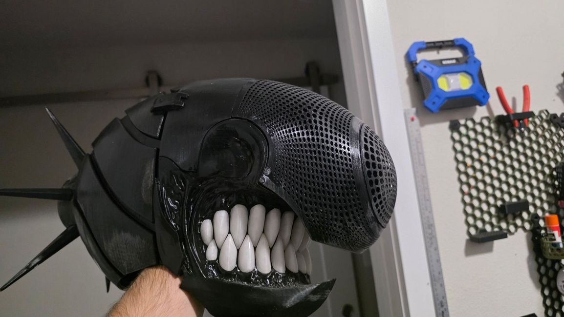 Side view of a black 3D-printed cosplay helmet with a perforated dome and rows of white teeth