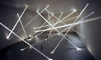 People walk through an art installation featuring glowing, crisscrossing light beams in a large, dark-walled gallery.