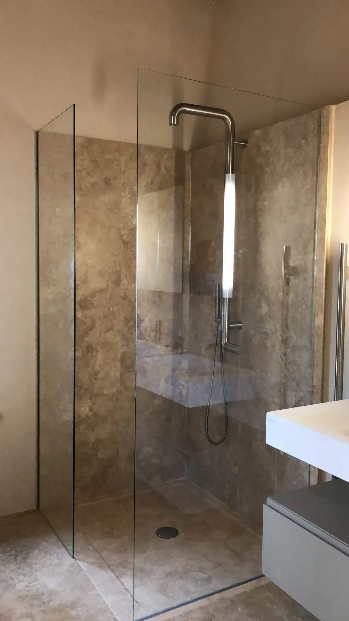 Bagno moderno con box doccia in vetro trasparente, pareti rivestite in piastrelle di pietra e bordo del lavabo bianco.
